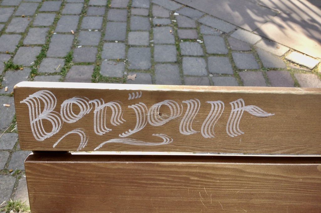 Bonjour-Graffiti auf einer Parkbank